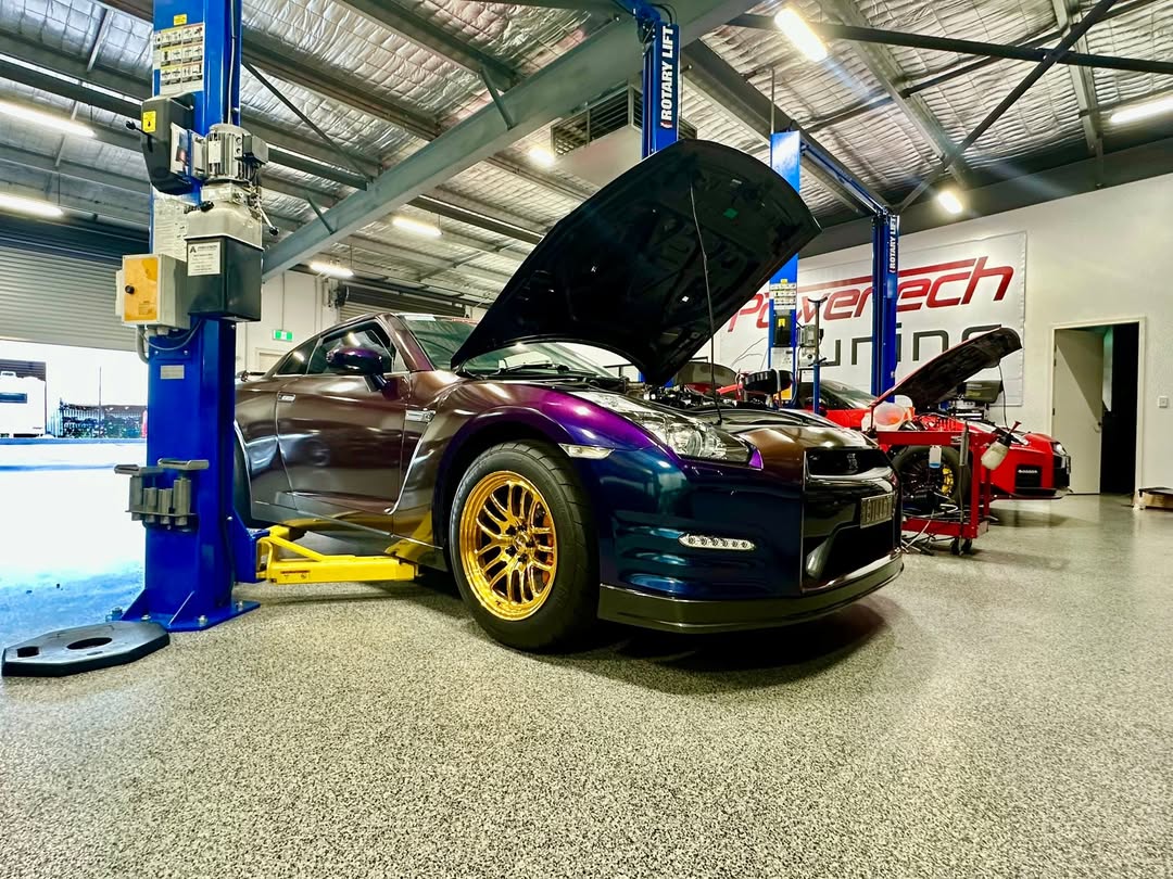 The Power Tech Tuning R35 GT-R roll racing car on the hoist in front of the workshop wall banner