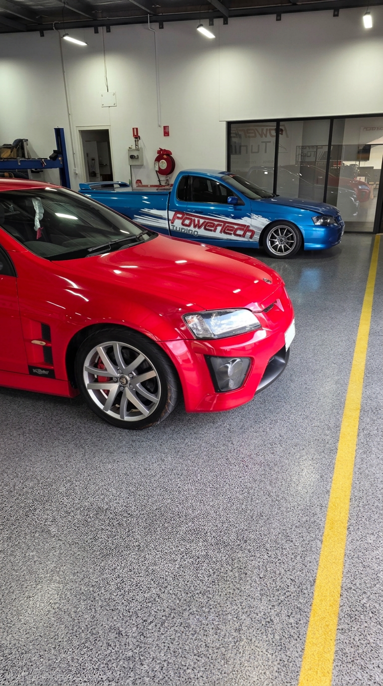 Red HSV sedan beside the blue Power Tech Tuning Falcon ute inside the workshop