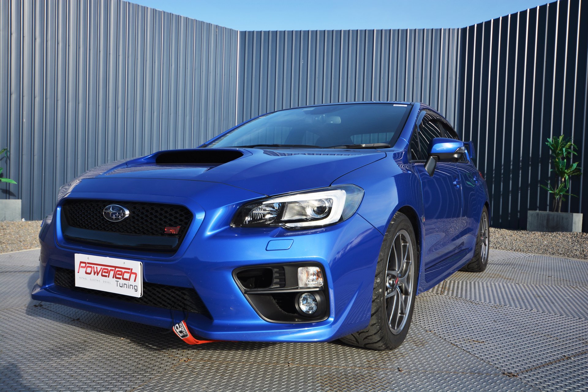 Blue Subaru WRX STI with a Power Tech Tuning trade plate outside the workshop